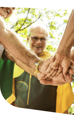 Elderly Man Smiling While Joining Hands With Friends Outdoors in Independent Living Elderly Man Smiling While Joining Hands With Friends Outdoors in Independent Living