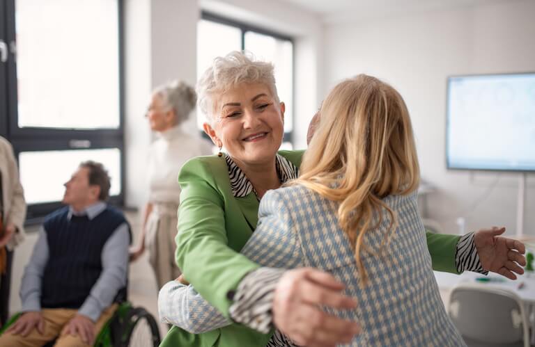 Smiling Elderly Woman Greeting a Friend With a Warm Hug in Independent Living