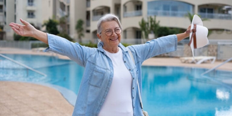 Joyful Elderly Woman with Arms Outstretched beside the Pool at Independent Living Facility